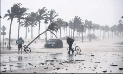  ??  ?? Two men walks their bicycle along a flooded street on the waterfront of Fort Lauderdale, Fla., as Hurricane Irma passes through on Sunday.