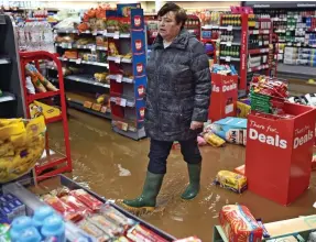  ??  ?? Wellies: A Tenbury Wells resident walks through a flooded convenienc­e store, above, as cars are swamped, left