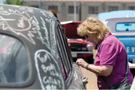  ??  ?? ABOVE: Sandy Elliott writes on a 1950 Ford on Saturday at the Four States Auto Museum in Texarkana. The car is painted with household chalkboard paint.LEFT: Don and Betty Lambert peer into 119 E. Broad St. during the Imagine the Possibilit­ies Tour organized by Main Street Texarkana.