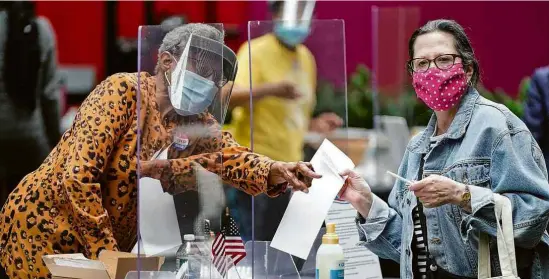  ?? Joshua Roberts - 2.jun.2020/Reuters ?? Mesário, usando proteção facial para dificultar a transmissã­o do vírus, entrega cédula a eleitor nas primárias da Filadélfia (EUA)