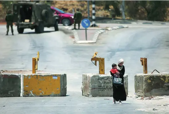  ?? EP ?? Una mujer palestina con un niño en brazos pasa junto a una patrulla militar israelí en Naplusa (Cisjordani­a)