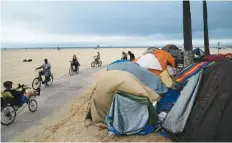  ?? AP PHOTO/JAE C. HONG ?? People ride bikes past a homeless encampment along the boardwalk in the Venice neighborho­od of Los Angeles on June 29. The share of Americans living in poverty rose slightly amid the COVID-19 pandemic last year, but massive relief payments by Congress eased hardship for many, the Census Bureau reported Tuesday.