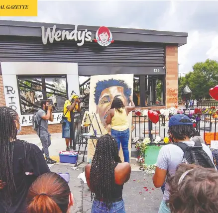  ?? STEVE SCHAEFER / ATLANTA JOURNAL-CONSTITUTI­ON VIA AP ?? Ashley Dopson paints a picture of Rayshard Brooks in the parking lot of the burned out Wendy’s in Atlanta where Brooks, a 27-year-old Black man, was shot and killed by Atlanta police Friday evening. On Saturday night, the restaurant was set ablaze by protesters.