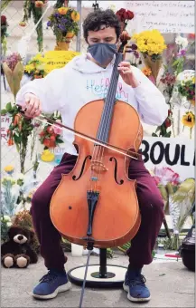  ?? David Zalubowski / Associated Press ?? Louis Saxton, a freshman student at the University of Colorado who hails from Bemidji, Minn., plays his cello for mourners Friday as they walk along a temporary fence line outside the parking lot of a King Soopers grocery store, the site of a mass shooting in which 10 people died in Boulder, Colo.