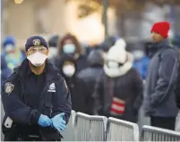  ?? (Stefan Jeremiah/Reuters) ?? A NYPD POLICEMAN puts on gloves yesterday as people wait in line to be tested for coronaviru­s outside Elmhurst Hospital Center in the borough of Queens.