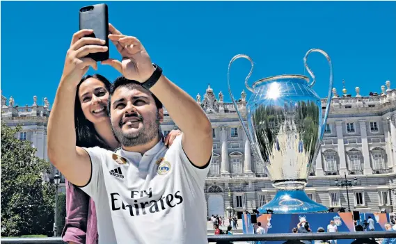  ??  ?? Photo opportunit­y: Fans pose near a huge replica of the Champions League trophy, but Madrid is on anti-terrorism alert and braced for a supporter invasion