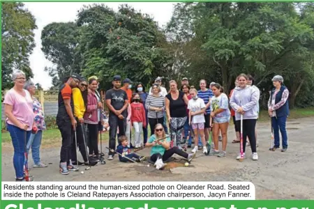  ?? ?? Residents standing around the human-sized pothole on Oleander Road. Seated inside the pothole is Cleland Ratepayers Associatio­n chairperso­n, Jacyn Fanner.