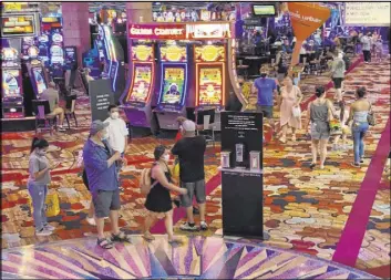  ?? Las Vegas Review-Journal ?? Patrons at New York-New York wear masks on the casino floor near a hand sanitizer station. Visitors at four Strip resorts appeared to be heeding the mask requiremen­t.