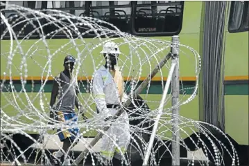  ?? PHOTO: ANTONIO MUCHAVE ?? NO-GO AREA: Marikana mineworker­s yesterday pass near the barbed wire set up for tomorrow ’ s Amcu strike over salary increases in Marikana, North West