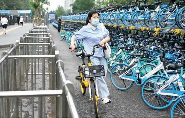  ?? Agence France-presse ?? ↑
A woman pushes a ride-sharing bicycle along a road past racks of bicycles in Beijing on Monday.