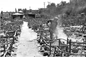  ??  ?? In this file photo an Afghan man shovels debris after Taliban militants burned a market in Ghazni. — AFP photo