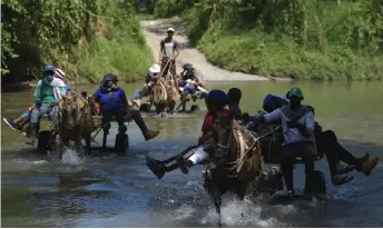  ?? — AFP photo ?? Haitian migrants cross the river on horse-drawn wagons before heading to the border with Panama in Acandi, Colombia.