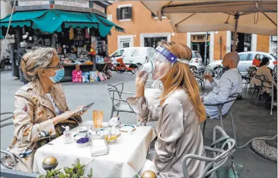  ?? Cecilia Fabiano The Associated Press ?? A woman sips her coffee from under her facial protection Monday at a cafe with outdoor tables in Rome.