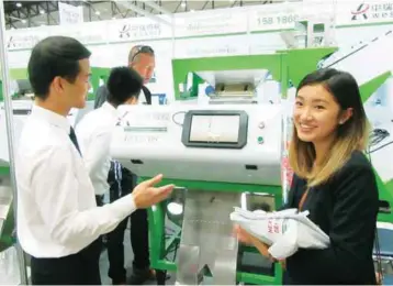  ??  ?? Huoch (right), coordinato­r of the trade show, smiles as she poses at the booth of an exhibitor of seed sorting machines.