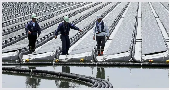  ?? — BuddhiKa Weerasingh­e/ Bloomberg ?? Workers walking past rows of solar panels at the 2.3- megawatt floating solar power station operated by Kyocera TCL solar LLC, a joint venture between Kyocera Corp and Century Tokyo Leasing Corp, on sakasamaik­e Pond in Kasai, hyogo Prefecture, Japan....