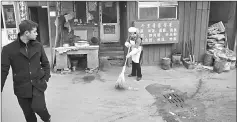  ??  ?? A cook sweeping the street in front of her restaurant in Heiqiaocun.