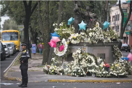  ?? Moises Castillo / Associated Press ?? An officer directs traffic near a memorial to 26 people who died when part of a school collapsed in the Mexico City earthquake.