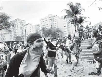  ??  ?? Opositores lanzan piedras a la policía, que dispersa con bombas de gas lacrimógen­o las movilizaci­ones en Caracas contra el gobierno de Nicolás Maduro ■ Foto Afp