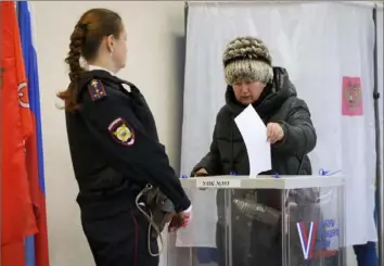  ?? Dmitri Lovetsky/Associated Press ?? A woman casts a ballot Sunday as a police officer guards a polling station during the presidenti­al election in St. Petersburg, Russia. Voters went to the polls for the last day of an election that extended President Vladimir Putin’s rule for another six years.