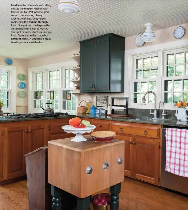  ??  ?? Beadboard on the walls and ceiling infuses the modern kitchen with farmhouse flair. Pat intermingl­ed some of her existing cherry cabinets with new deep-green cabinets with a red rub-through finish. She painted the legs on the vintage butcher block to match. The light fixtures, which are salvage finds, feature a similar shape but different colors. A weathered grain bin disguises a wastebaske­t.