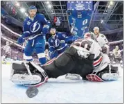  ?? Bruce Bennett Associated Press ?? LIGHTNING’S J.T. Brown, left, watches as Cedric Paquette’s shot goes by Blackhawks’ Corey Crawford.