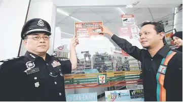  ??  ?? Sum (left) and Abdul Khairi showing the Safecam PDRM-7-Eleven MoU sticker at the Taman Tasik Indera 7-Eleven store. — Bernama photo