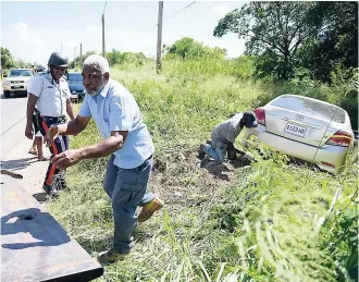  ?? GLADSTONE TAYLOR PHOTOS ?? Tow truck operators and a police officer on the scene of an accident along the Toll Gate main road in Clarendon last Friday. A Toyota Allion sedan lost control and ran off the road. The injured driver was taken to seek medical attention.