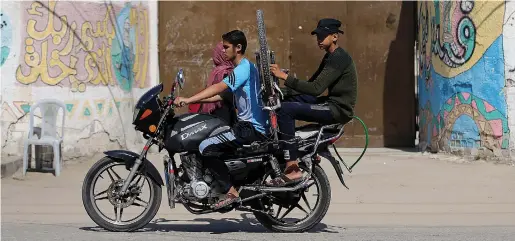  ?? (Ibraheem Abu Mustafa/ Reuters) ?? YOUTHS RIDE a motorcycle past a closed school in the southern Gaza Strip in May.