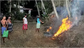  ??  ?? A young woman lights a fire beside her home to keep both elephants and mosquitoes at bay