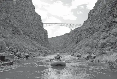  ?? TINA LARKIN/TAOS NEWS FILE PHOTO ?? Los Ríos River Runners raft guide Nathan Oswald heads down the Rio Grande toward the Gorge Bridge. The Rio Grande National Monument stretches across 242,500 acres up the Rio Grande Gorge, far past its landmark bridge, to the Colorado line and west...