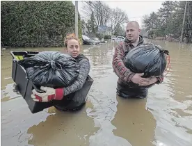  ?? RYAN REMIORZ THE CANADIAN PRESS ?? Residents Lawrence Courville, left, and Andie Goulet carry out belongings down a flooded street in Ste-Marthe-sur-le-Lac, Que., on Sunday.