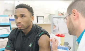  ?? MICHAEL BELL ?? Roughrider­s linebacker Jeff Knox Jr. gets a flu shot from pharmacist Brent Goeres at the Victoria Square Mall Shoppers Drug Mart. Knox is helping promote public flu awareness this year.