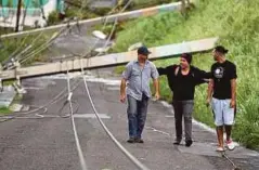  ??  ?? TIGA lelaki berjalan berhampira­n tiang elektrik yang tumbang di Luquillo, Puerto Rico kelmarin. - AFP