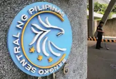  ?? — Reuters ?? A security guard stands beside a logo of the Central Bank of the Philippine­s posted at the main gate in Manila.