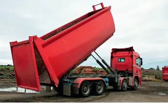  ??  ?? The truck driver sets the bin down on a skid site for loading with woody residue – the previous barn door design was changed for a top-swinging design and works much better.