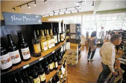  ?? LUIS SÁNCHEZ SATURNO/THE NEW MEXICAN ?? Local wines sit on the shelves at Kaune’s Neighborho­od Market as people wait in line Tuesday at the registers.