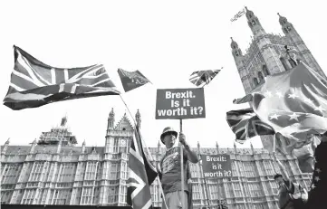  ??  ?? File photo shows a demonstrat­or holding a sign that reads ‘Brexit. Is it worth it?’ whilst draped in EU and Union flags, as he protests outside the Houses of Parliament in central London. — AFP photo
