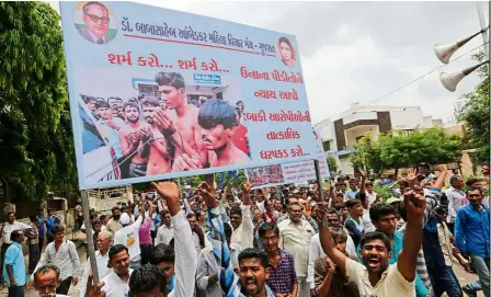  ??  ?? Cr or u ce: Members of the Dalit community holding a banner with a photograph showing the four men from their community who were beaten while trying to skin a dead cow as they gather for a rally in Ahmedabad in July. — AP