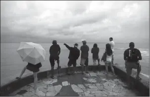  ?? The Associated Press ?? LOOKING OUT: People look out over the ocean along Waikiki Beach in a light rain from Tropical Storm Lane on Saturday in Honolulu. Lane, once known as Hurricane Lane, began to break apart as it veered west into the open Pacific, leaving behind sighs of relief and plenty of clean-up, especially on the Big Island where rainfall totals approached 4 feet.