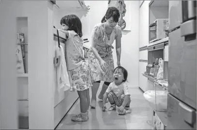  ?? [ANDREA DICENZO/THE NEW YORK TIMES] ?? Working mother Yoshiko Nishimasa reaches out to console her son after he had an accident while playing in the kitchen. Her husband rarely gets home from work before 10 p.m. On Saturdays, he sleeps in while his wife shuttles the three children to activities.