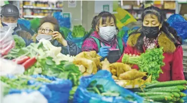  ?? (AFP) ?? People wearing protective masks buy vegetables in Hangzhou in China’s eastern Zhejiang province on Monday