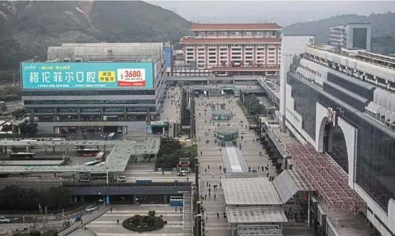  ?? — ©2024 The new york Times Company ?? a large video screen displays an ad for a dental clinic where implants cost Us$500, at luohu port. (left) Hong Kong residents partaking in a seafood hot pot at a restaurant in shenzhen, China. Hong Kong residents are finding in shenzhen, lower prices, better service and tasty cuisine.