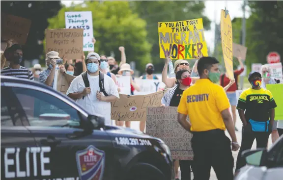  ?? DAX MELMER ?? Demonstrat­ors rallying in support of migrant agricultur­al workers toiling on area farms are met by security personnel outside Lakeside Produce in Leamington on Sunday.