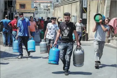  ?? HASAN SHAABAN / GETTY IMAGES ?? Residents carry empty cooking gas cylinders to refill in Beirut, Lebanon, on Tuesday. Lebanon’s fuel crisis has exacerbate­d power blackouts and resulted in long lines at gasoline stations during the nation’s worst financial meltdown in memory.