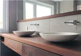  ??  ?? Wood shelving and trim add a bit of warmth to the Zen-like decor of this bathroom, with its freestandi­ng tub and above-counter stone vessel sinks, and metal fixtures. Minimalist decor need not mean a cold look.