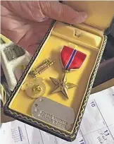  ??  ?? Bretton holds his Bronze Star, along with other decoration­s and his dog tag from World War II.