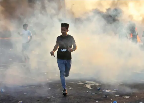  ?? AFP ?? Iraqi demonstrat­ors run amidst smoke from burning tires during a rally against state corruption, failing public services, and unemployme­nt, in Baghdad.