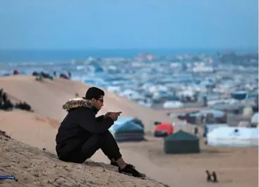  ?? ?? a displaced Palestinia­n using an esim card attempts to get a signal in order to contact his relatives on a hill in rafah, on the southern Gaza Strip on the border with Egypt. — AFP