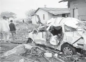  ??  ?? Men walk past the wreckage of a car following the tsunami in Palu.