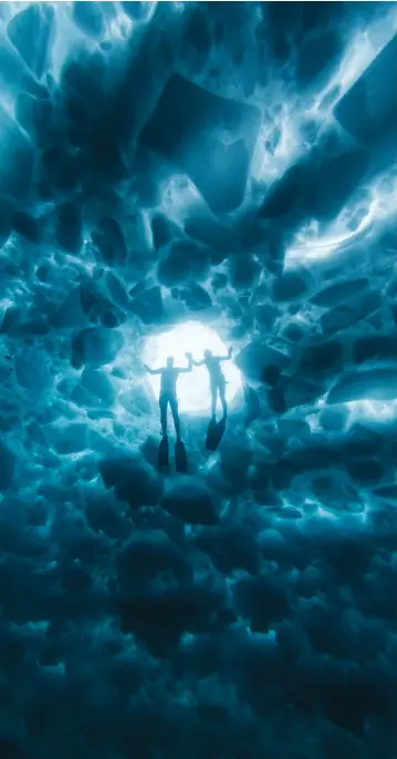  ??  ?? Clockwise from opposite, bottom left:
Ryzebol carries his fins after emerging from the water; Ryzebol examines the wreck of the Alice G; Ryzebol stands atop a 2.5-metre-thick chunk of ice; Lily Tjeng (right) and Tyler Boelens hold hands while looking down into the water from a hole in the ice; a drone shot of Ryzebol at the edge of the bay’s expanse of ice; Ryzebol sits at the edge of a hole in the ice.